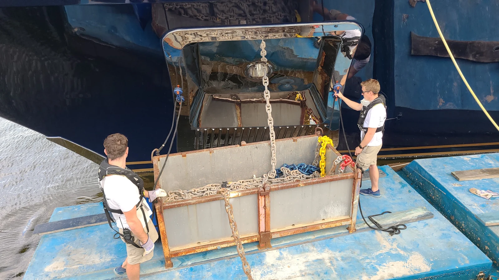 Crew handling a yacht anchor and chain from a floating work platform